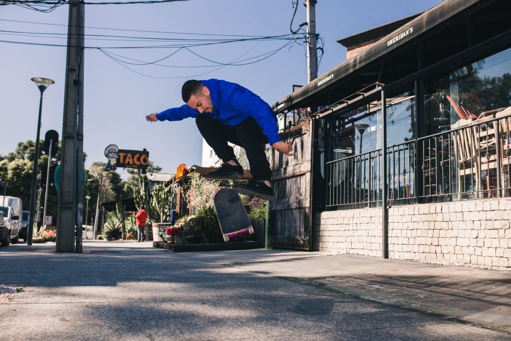 Homem portando jaqueta azul, executando manobra de skate